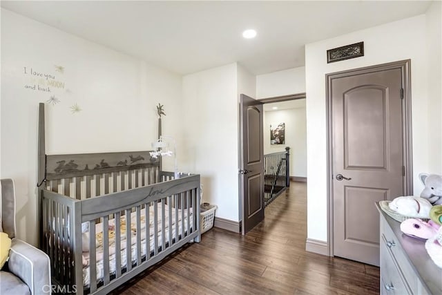 bedroom with a crib, baseboards, wood finished floors, and recessed lighting