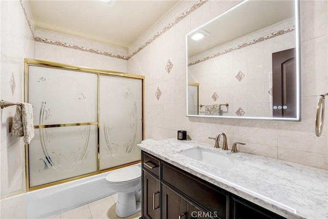 full bathroom featuring toilet, tile patterned flooring, combined bath / shower with glass door, vanity, and tile walls