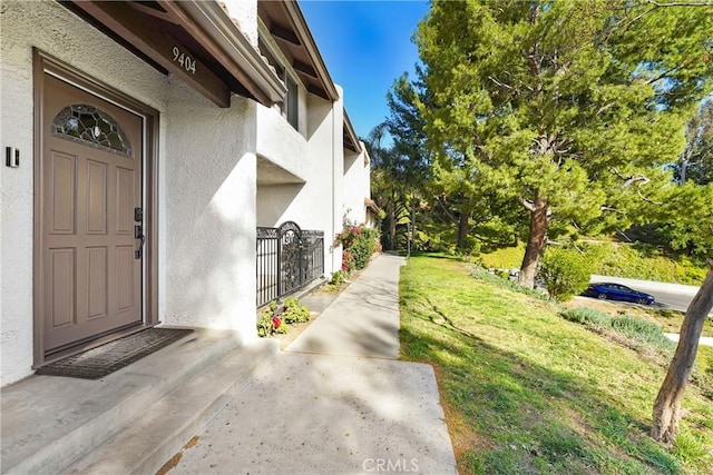 entrance to property featuring a lawn and stucco siding