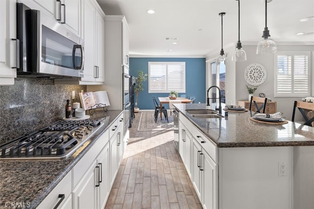 kitchen featuring tasteful backsplash, appliances with stainless steel finishes, ornamental molding, wood tiled floor, and a sink