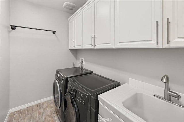 laundry room with cabinet space, light wood-style floors, washing machine and dryer, a sink, and baseboards