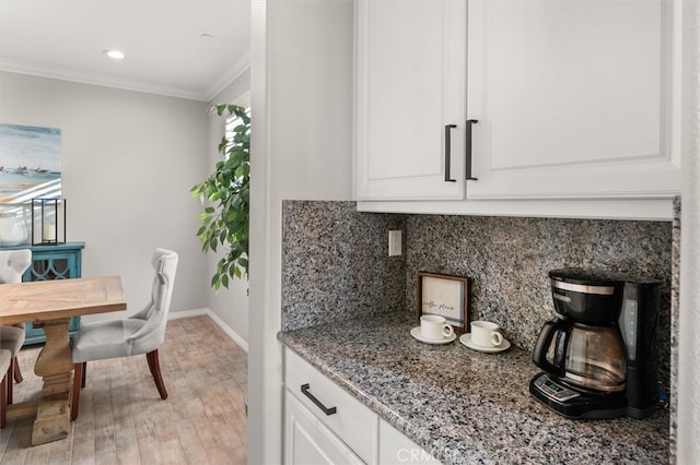 kitchen featuring stone countertops, light wood-style flooring, white cabinetry, backsplash, and crown molding