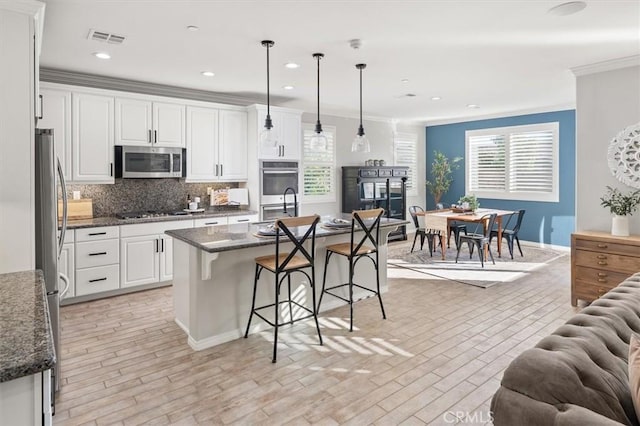 kitchen with white cabinetry, visible vents, a kitchen breakfast bar, appliances with stainless steel finishes, and decorative backsplash