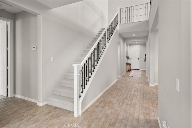 staircase featuring wood finished floors, a towering ceiling, and baseboards