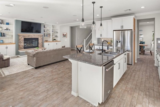 kitchen featuring a stone fireplace, a sink, visible vents, appliances with stainless steel finishes, and dark stone counters