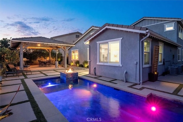 rear view of house with an outdoor fire pit, an outdoor pool, a gazebo, a patio area, and stucco siding