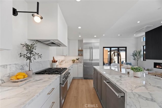 kitchen with a sink, white cabinetry, light wood finished floors, high end appliances, and custom range hood