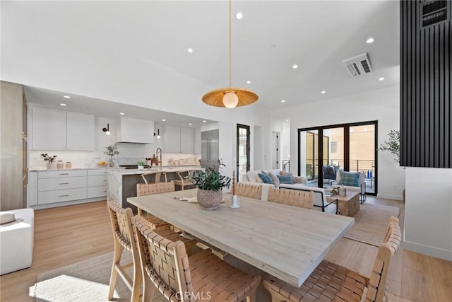 dining room with light wood-style flooring, a towering ceiling, visible vents, and recessed lighting