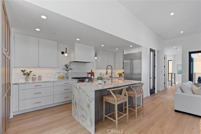 kitchen featuring stainless steel built in refrigerator, a kitchen bar, a sink, and light wood-style floors