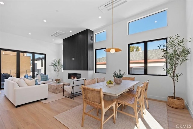 dining room featuring a large fireplace, baseboards, light wood-style flooring, and a healthy amount of sunlight