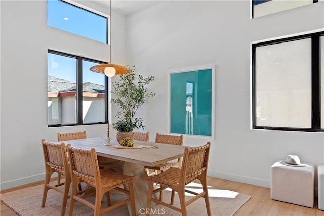 dining area with light wood-style floors, a high ceiling, and baseboards