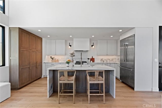 kitchen with a center island with sink, light stone countertops, light wood-style floors, high end fridge, and recessed lighting