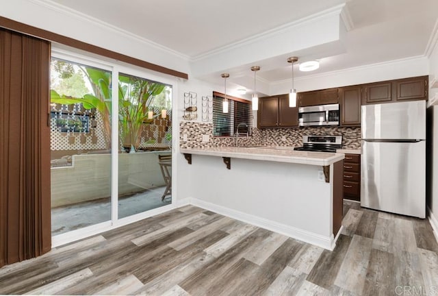 kitchen with dark brown cabinets, appliances with stainless steel finishes, a peninsula, and ornamental molding