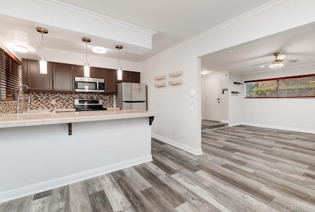 kitchen with a peninsula, ornamental molding, a sink, tile counters, and appliances with stainless steel finishes