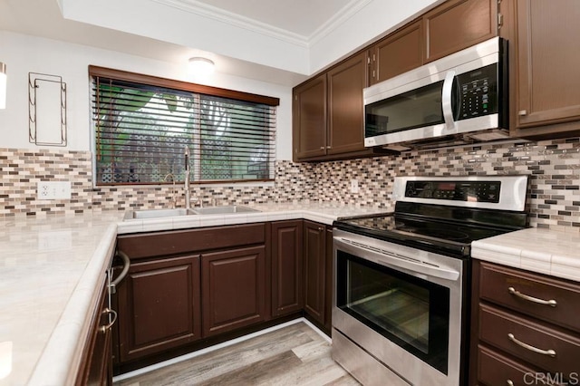 kitchen with a sink, stainless steel appliances, dark brown cabinets, and ornamental molding