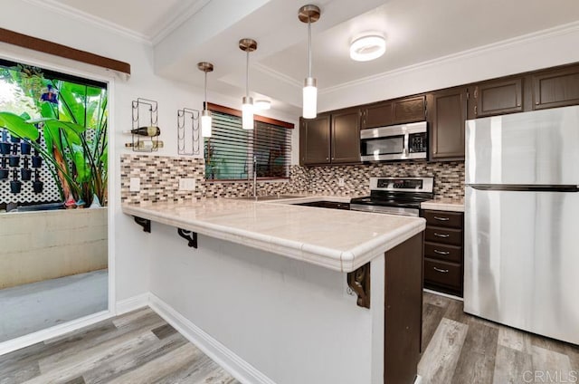 kitchen with a peninsula, a sink, stainless steel appliances, dark brown cabinets, and a kitchen bar