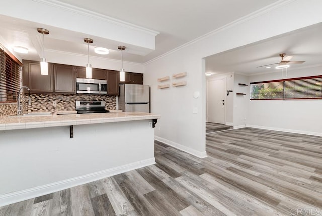 kitchen with tile counters, a sink, light wood-style flooring, a peninsula, and appliances with stainless steel finishes