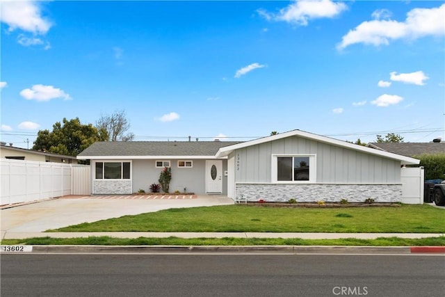 single story home featuring a front lawn, fence, stone siding, and driveway