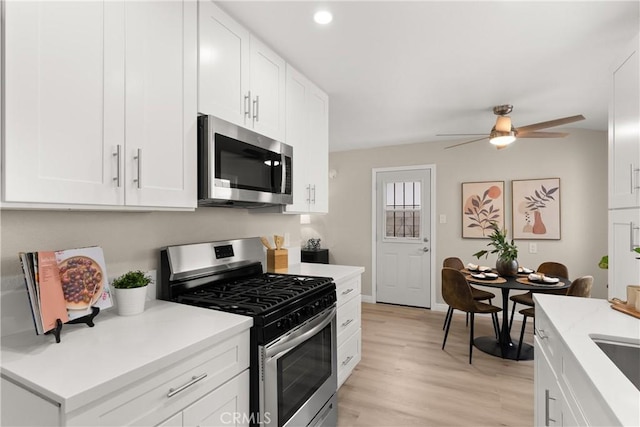 kitchen featuring light wood finished floors, light countertops, appliances with stainless steel finishes, white cabinetry, and a ceiling fan