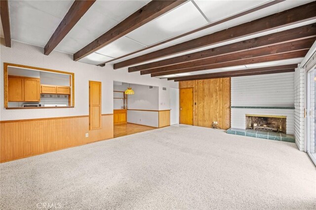 unfurnished living room featuring wainscoting, beamed ceiling, carpet flooring, wood walls, and a fireplace