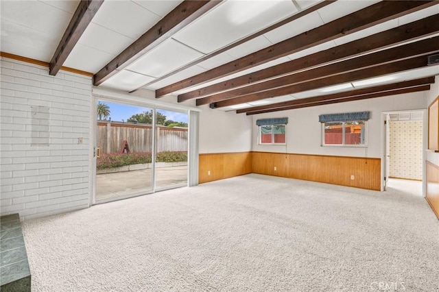 interior space with carpet, beam ceiling, a wainscoted wall, and wood walls