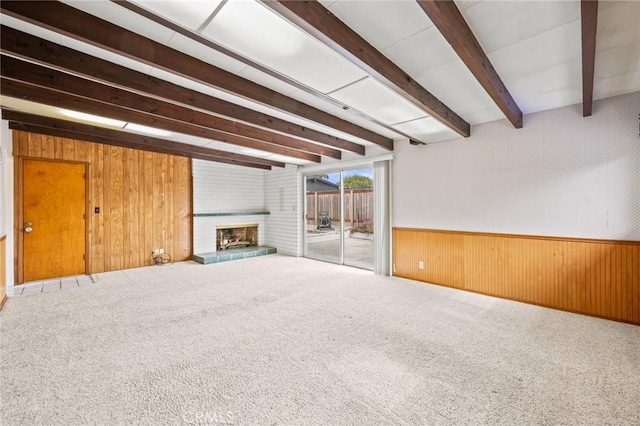 unfurnished living room with beam ceiling, a fireplace, wainscoting, carpet flooring, and wooden walls