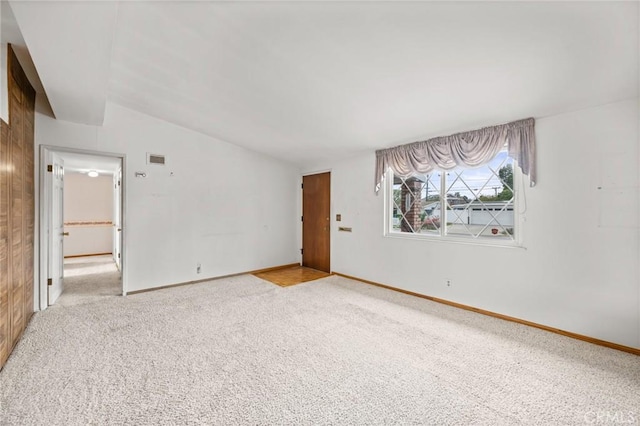 unfurnished room with baseboards, lofted ceiling, visible vents, and light colored carpet