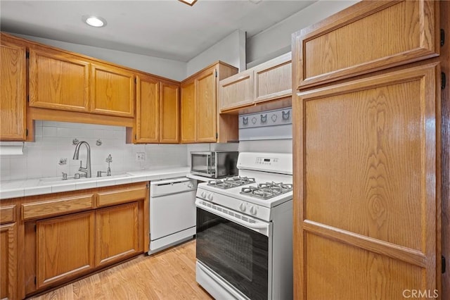 kitchen featuring tile countertops, white appliances, a sink, decorative backsplash, and light wood finished floors