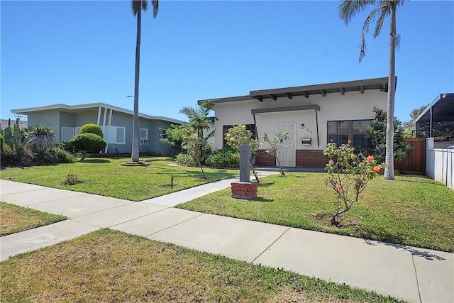 view of front of house with brick siding, fence, a front lawn, and stucco siding