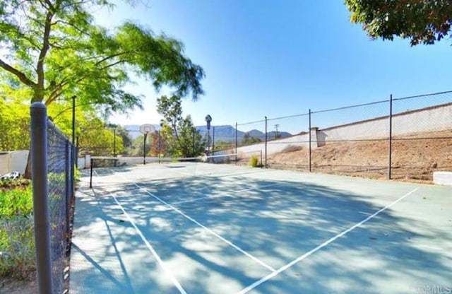 view of tennis court with community basketball court and fence