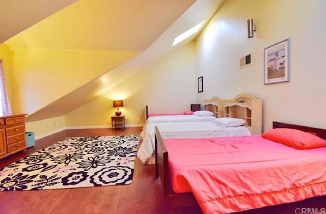 bedroom with vaulted ceiling with skylight, visible vents, baseboards, and wood finished floors