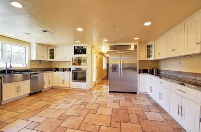 kitchen featuring dark countertops, glass insert cabinets, appliances with stainless steel finishes, a sink, and recessed lighting