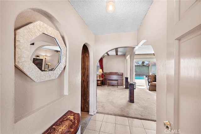 corridor with carpet floors, arched walkways, a textured ceiling, and tile patterned floors