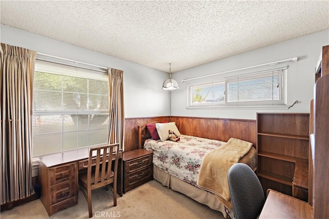 bedroom featuring light colored carpet, a textured ceiling, and wainscoting