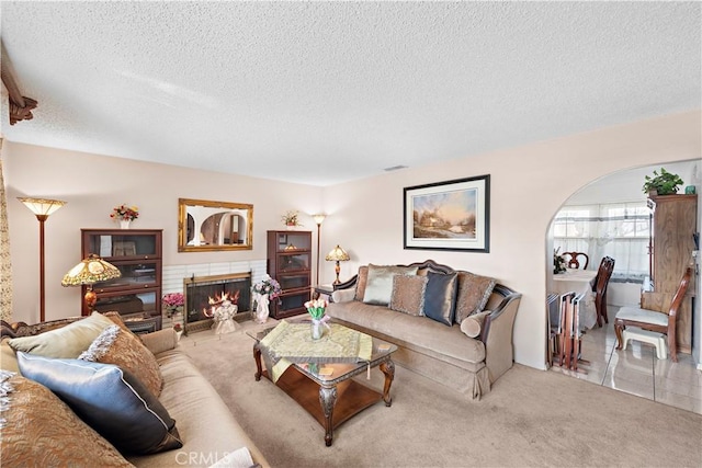 tiled living area with a warm lit fireplace, visible vents, arched walkways, carpet, and a textured ceiling