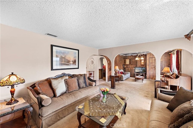 living room with carpet floors, arched walkways, visible vents, and a textured ceiling