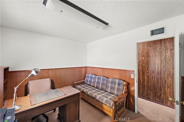 carpeted home office with a wainscoted wall, visible vents, wood walls, and a textured ceiling