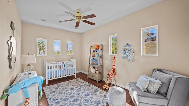 bedroom featuring a nursery area, ceiling fan, baseboards, and wood finished floors