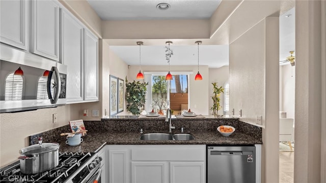 kitchen featuring stainless steel appliances, dark stone countertops, a sink, and white cabinetry