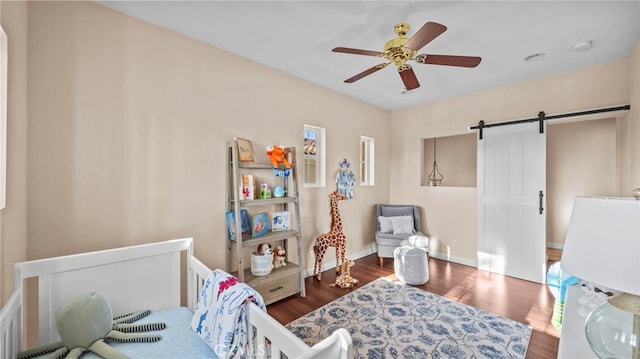 bedroom featuring a barn door, wood finished floors, a ceiling fan, and baseboards