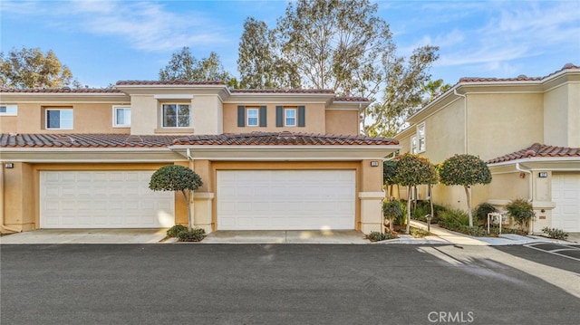 view of property featuring an attached garage, driveway, a tiled roof, and stucco siding