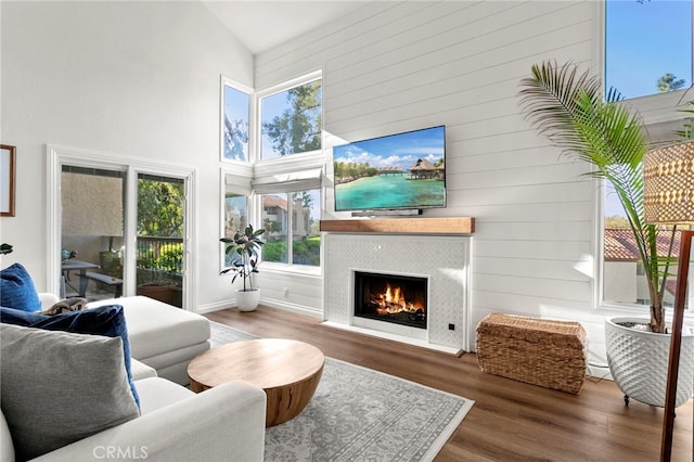 living area featuring a tile fireplace, high vaulted ceiling, a wealth of natural light, and wood finished floors