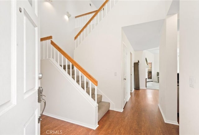 foyer entrance with stairs, wood finished floors, a towering ceiling, and baseboards