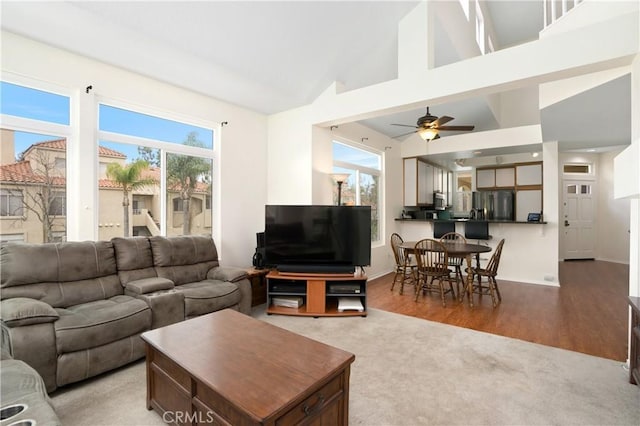 living area with carpet flooring, ceiling fan, wood finished floors, high vaulted ceiling, and baseboards