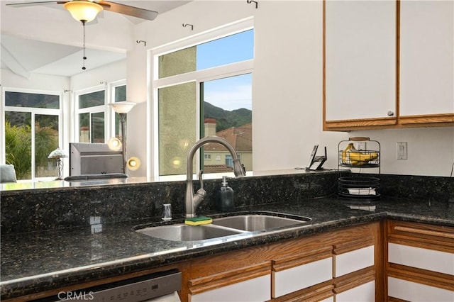 kitchen featuring ceiling fan, dishwashing machine, a sink, white cabinetry, and dark stone counters