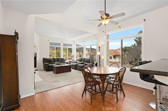 dining room featuring a healthy amount of sunlight, vaulted ceiling with beams, baseboards, and wood finished floors