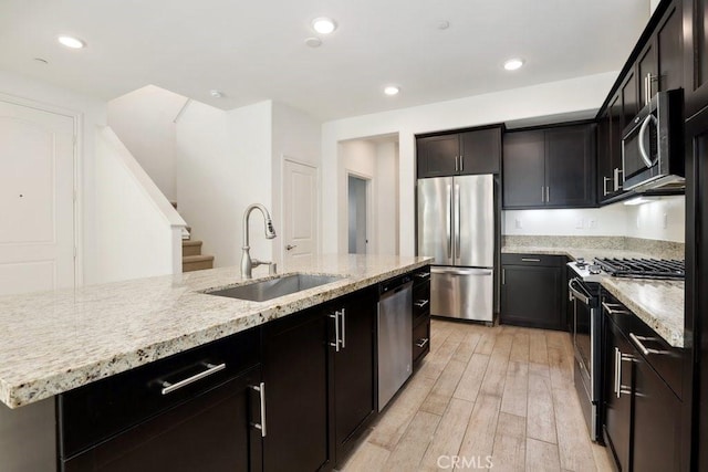 kitchen featuring light stone counters, stainless steel appliances, recessed lighting, light wood-style flooring, and a sink