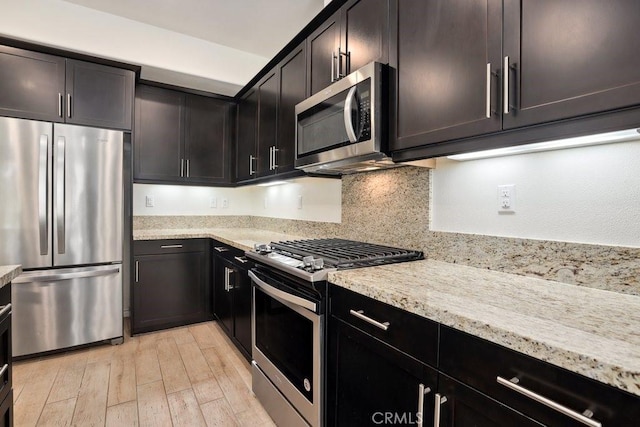 kitchen featuring light wood-type flooring, tasteful backsplash, appliances with stainless steel finishes, and light stone counters