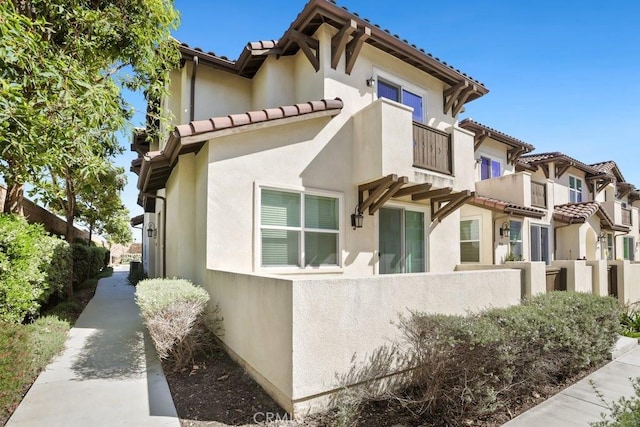 view of side of property featuring a tile roof, fence, a balcony, and stucco siding