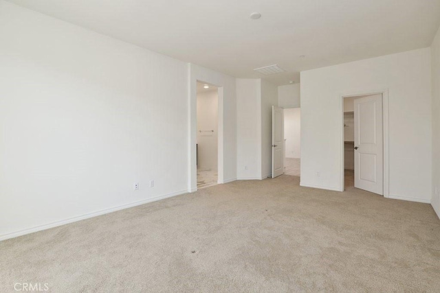 unfurnished bedroom with ensuite bathroom, light carpet, baseboards, a closet, and a walk in closet